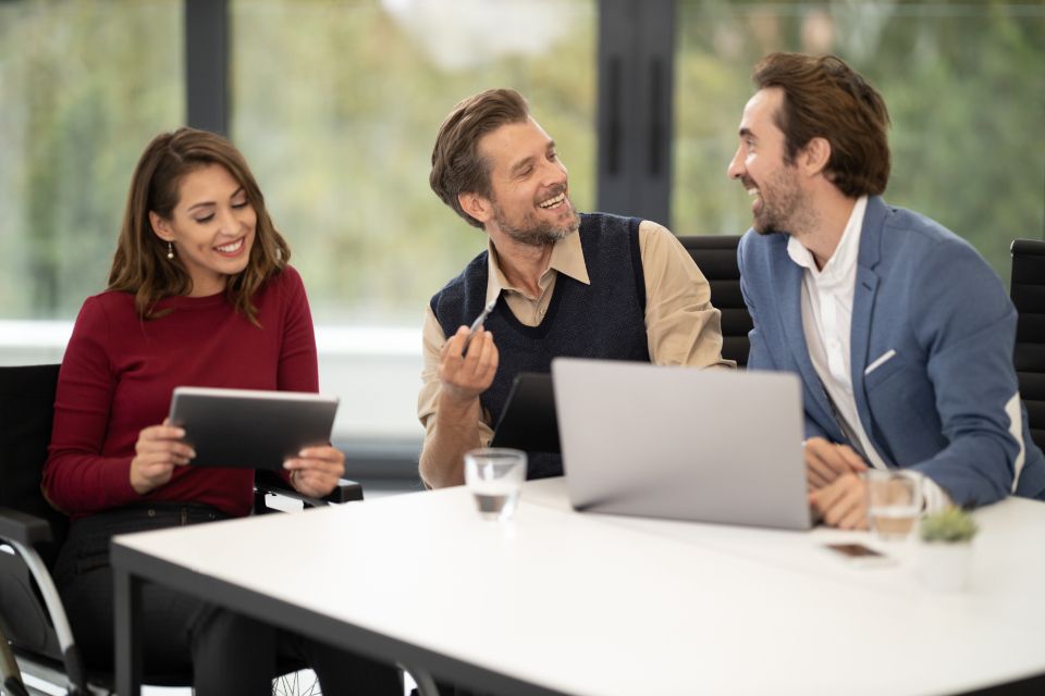 Tres profesionales conversando y sonriendo con una tablet y laptops en una mesa